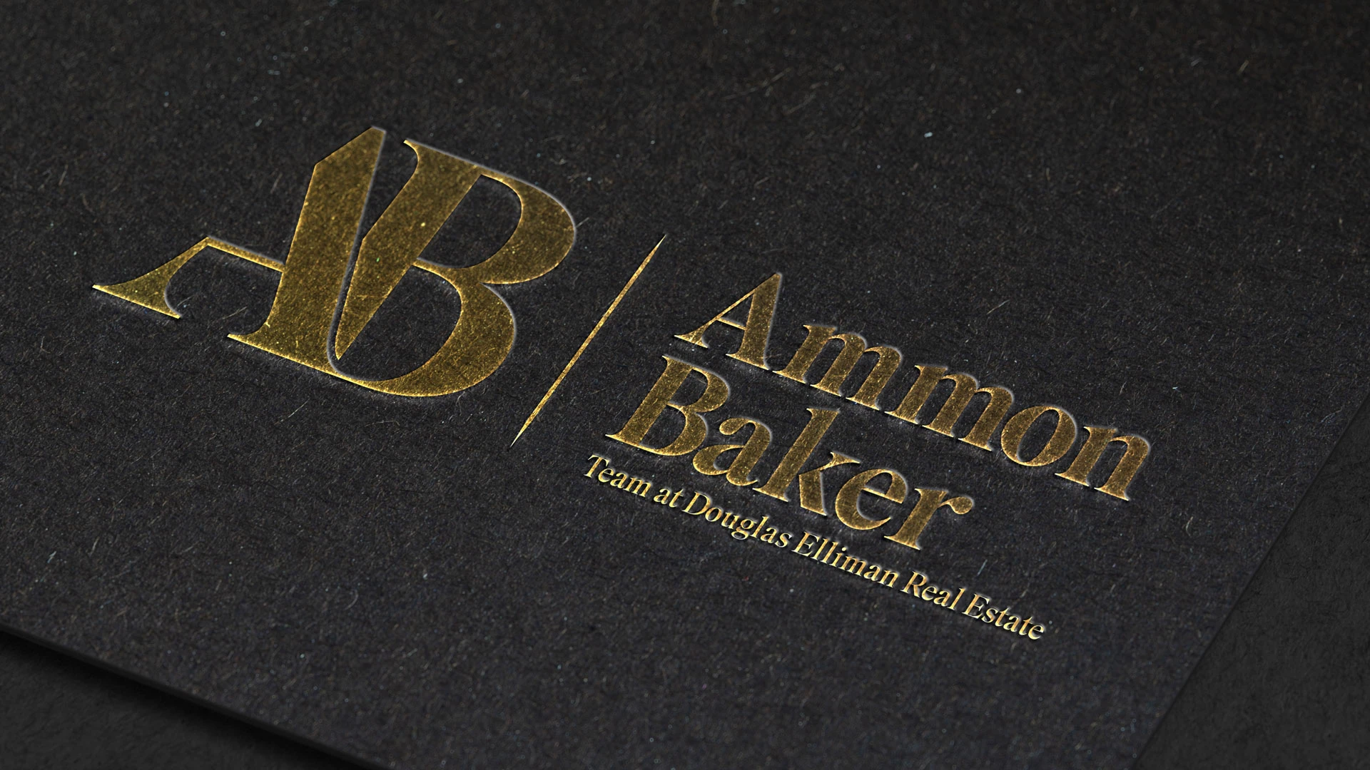Mockup of Ammon Baker brand identity, Option 3 in the left lockup as an embossed gold foil on dark paper.